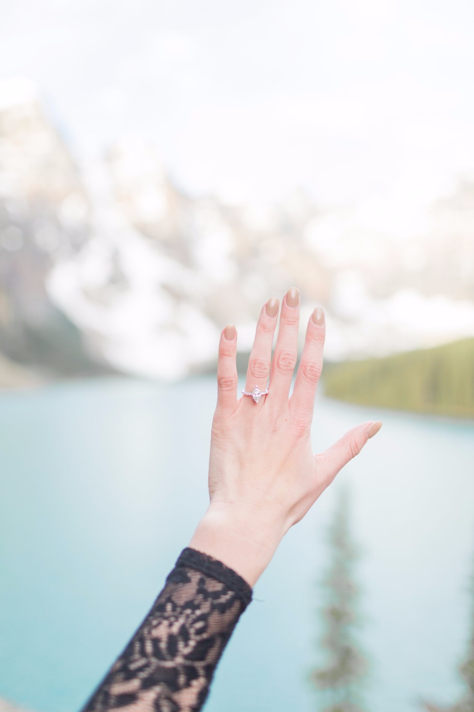 Woman shows engagement ring with mountain and lake background