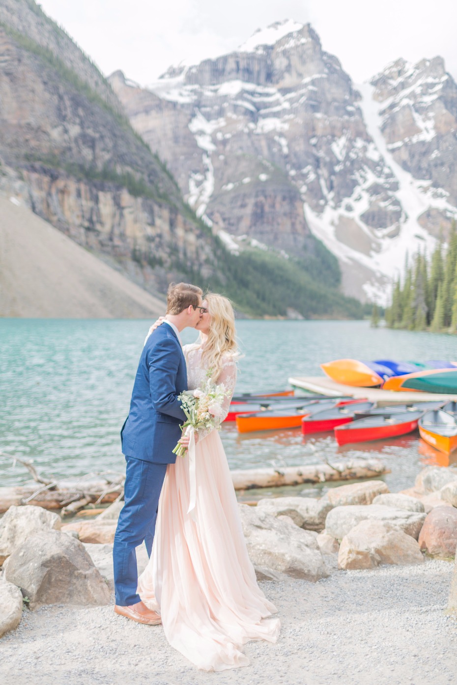 Couple kissing near a lake with mountains in the background