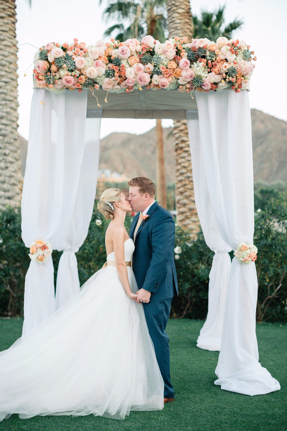 Bride and groom kiss under floral wedding archway