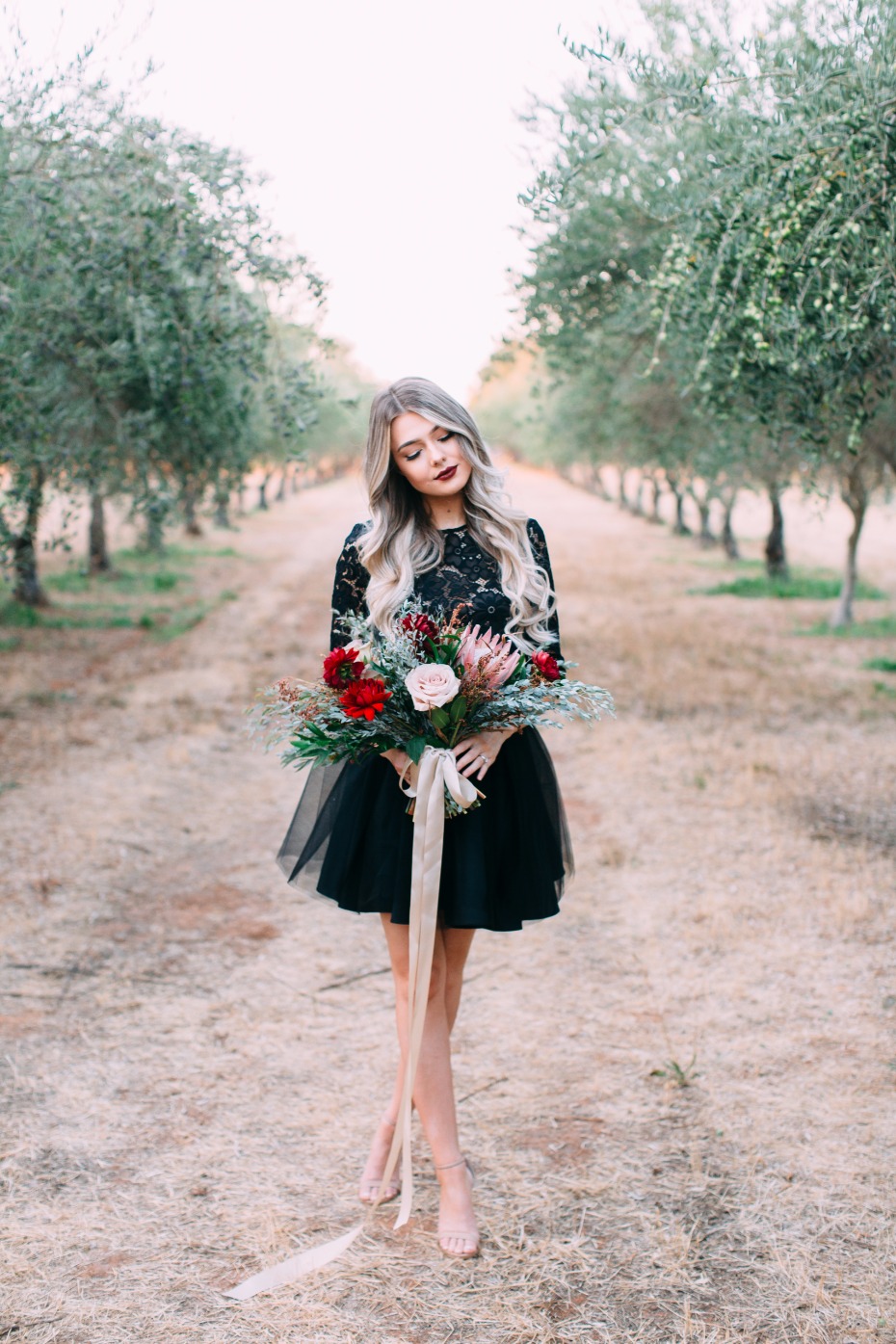 Woman with bouquet in black dress in olive tree field