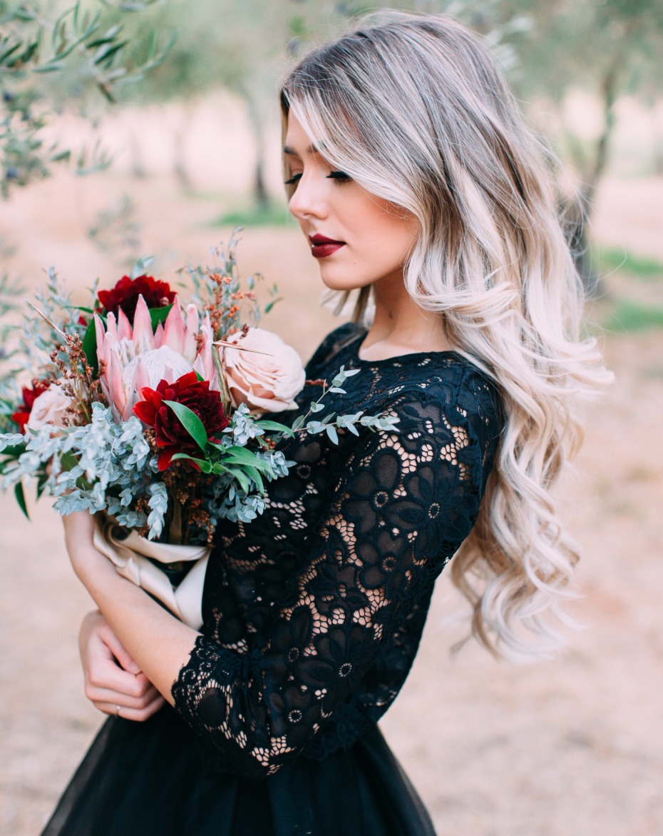 Blonde woman in lace dress holds floral bouquet outside