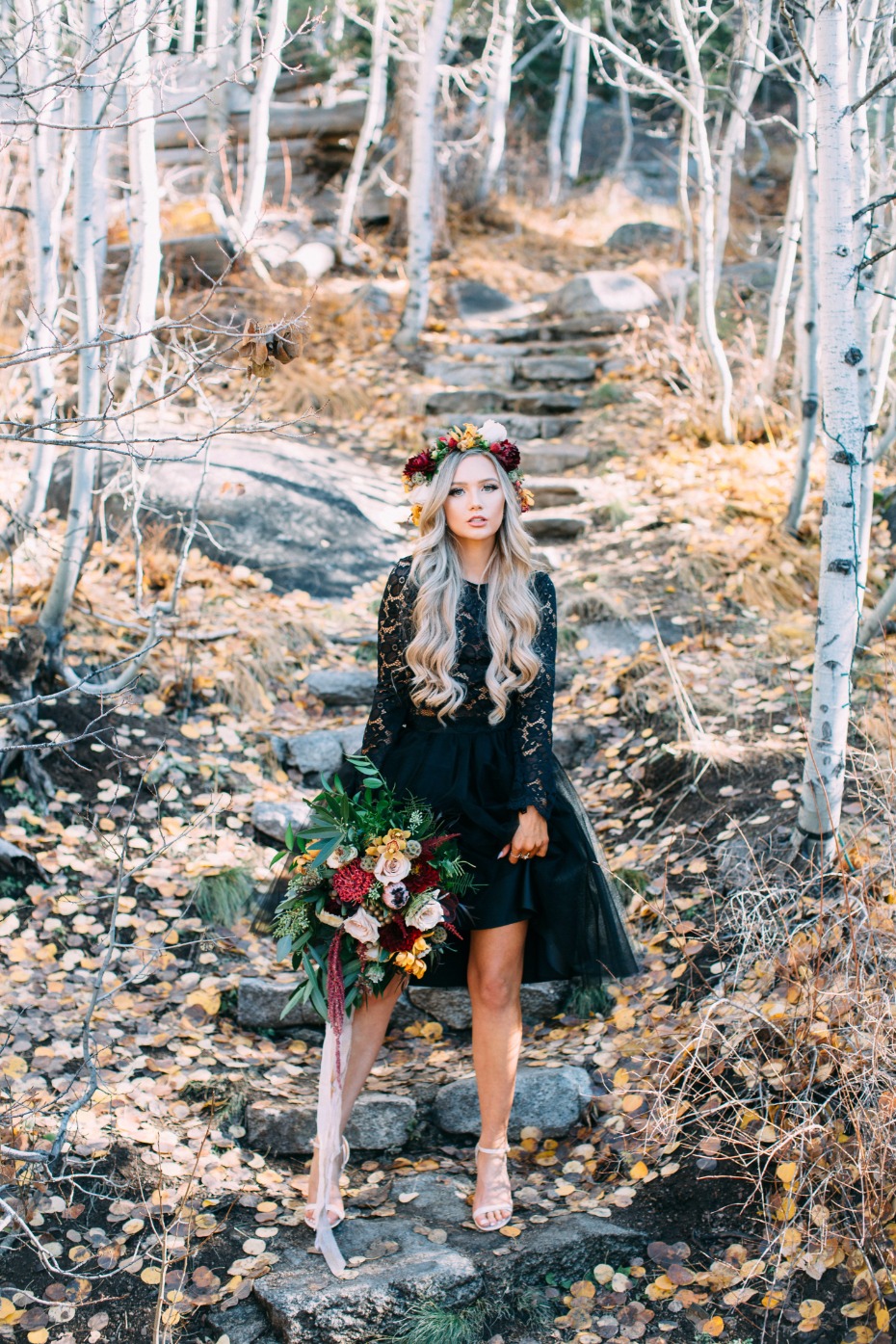 Woman in black dress with floral crown and bouquet in autumn woods