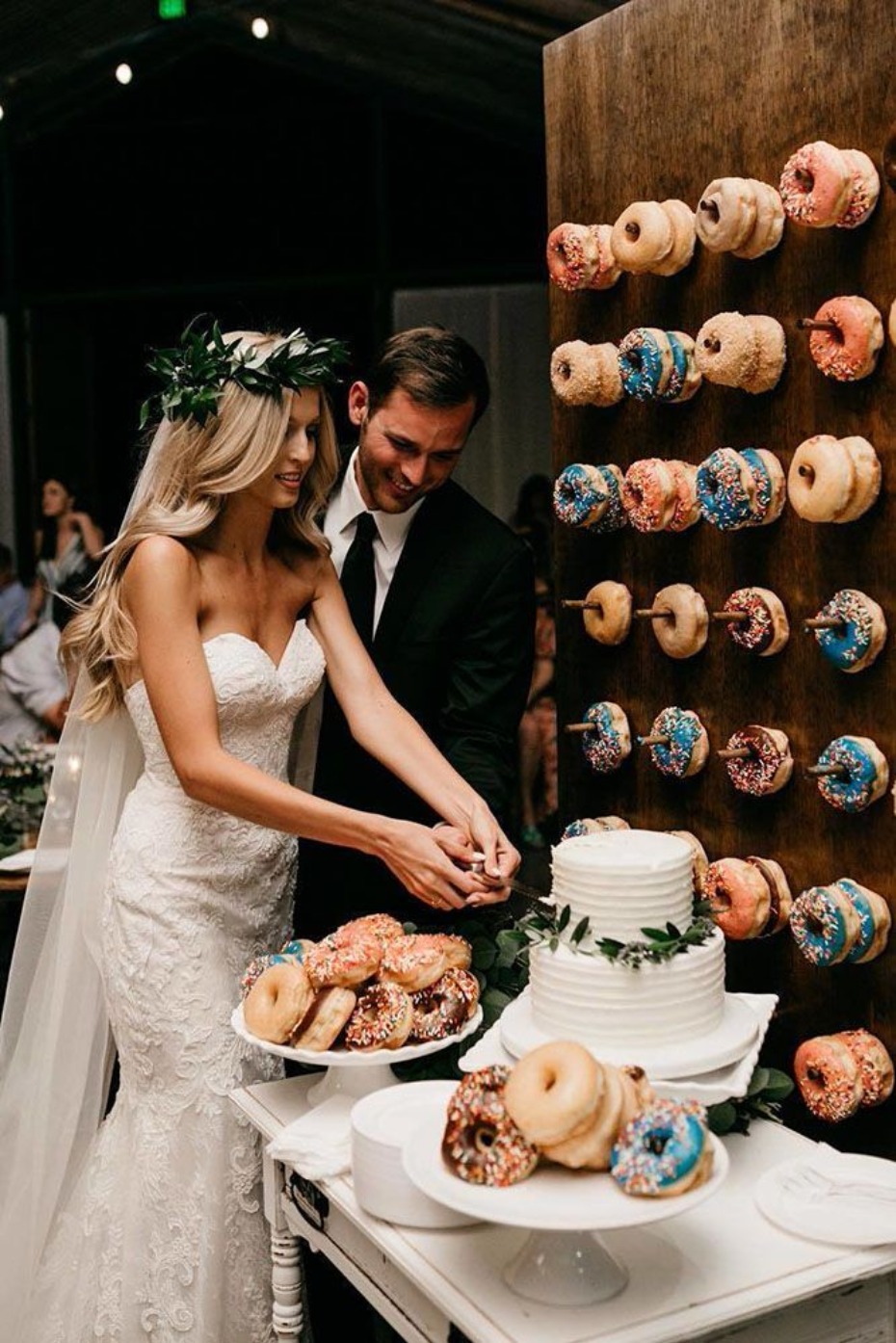 Bride and groom cutting cake by donut wall at wedding