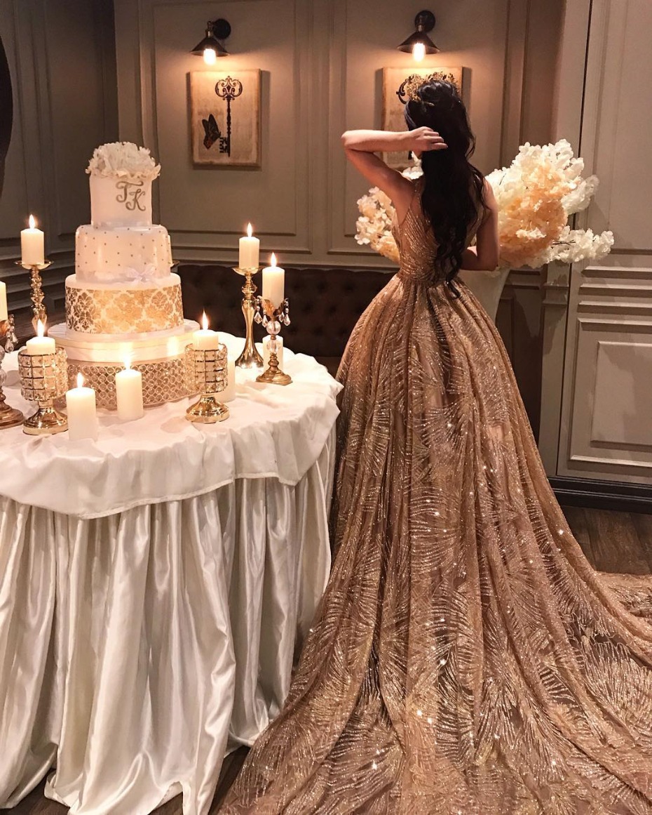 Woman in gold gown poses with wedding cake and candles