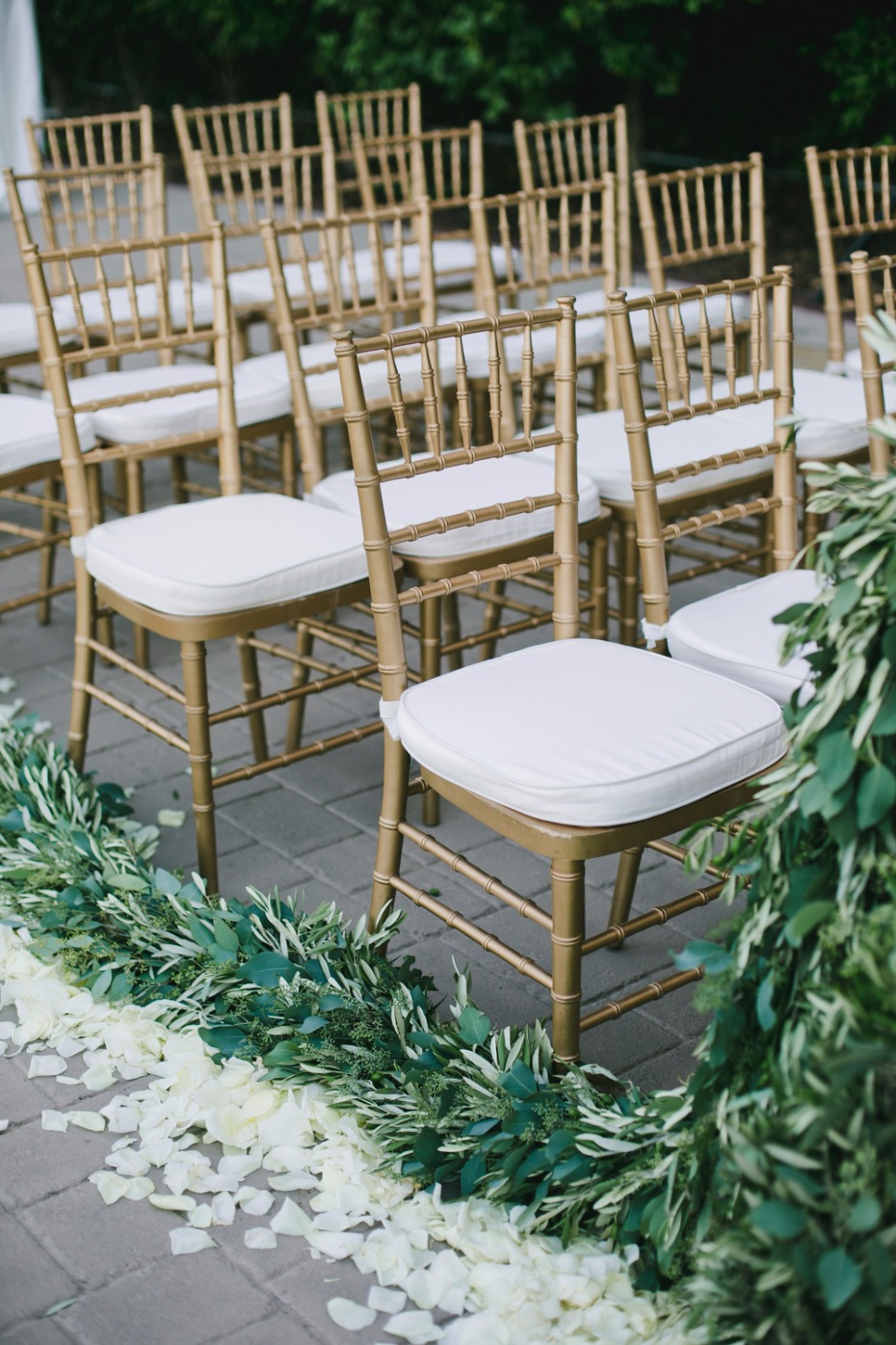 gold and white wedding chairs with greenery and white petal aisle decor