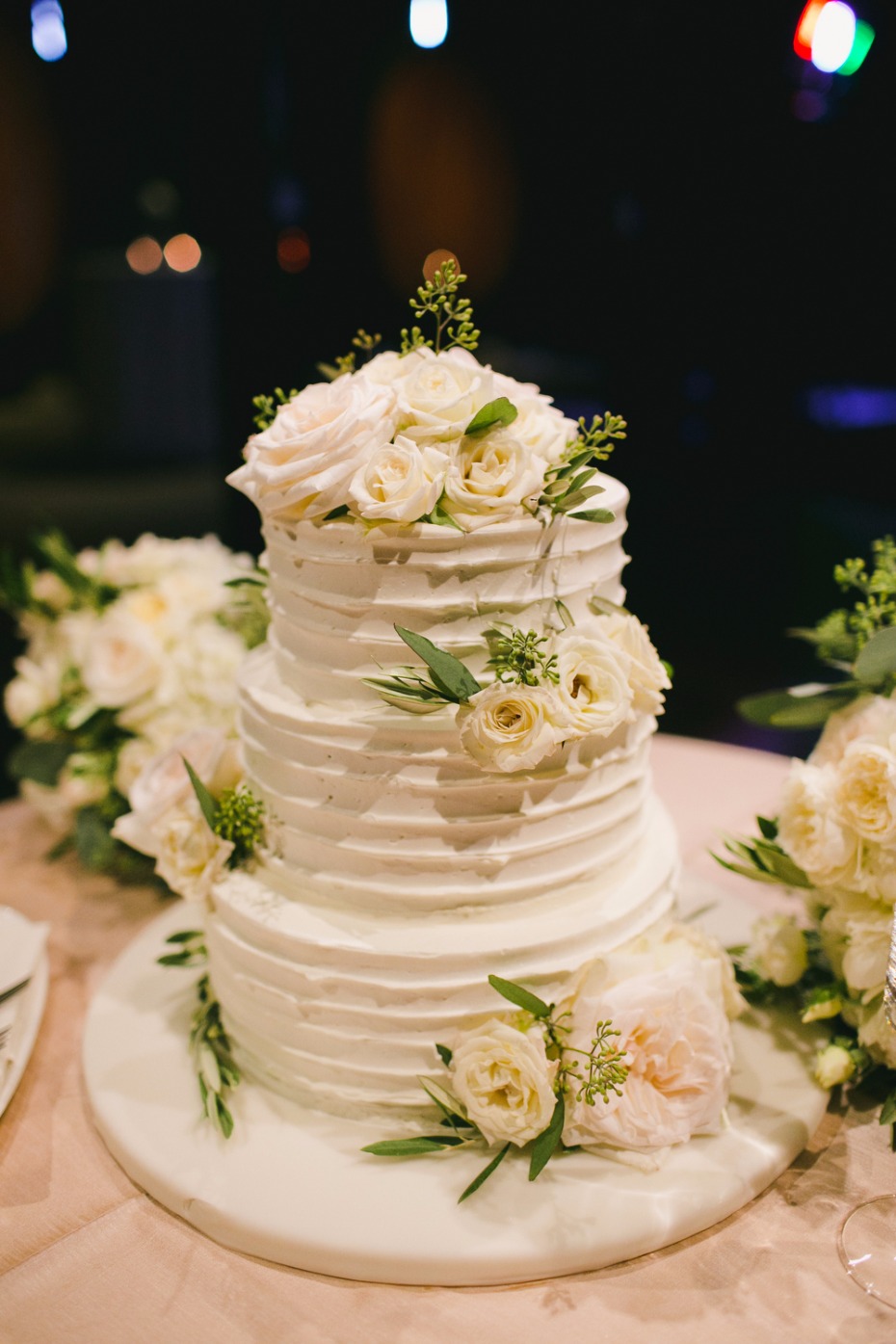 white wedding cake topped with roses and seeded eucalyptus