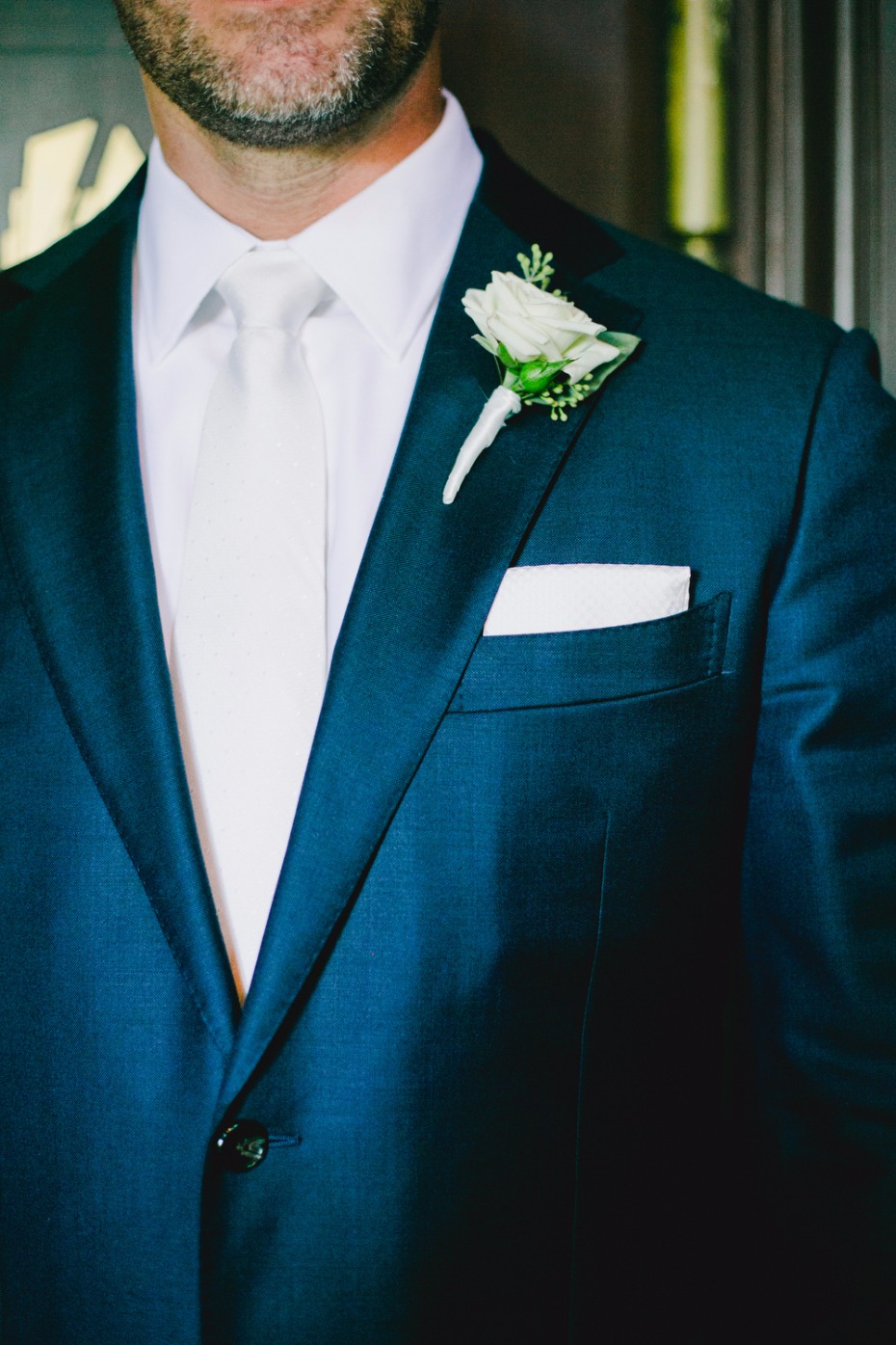 groom styled in blue suite white tie and white boutonniere