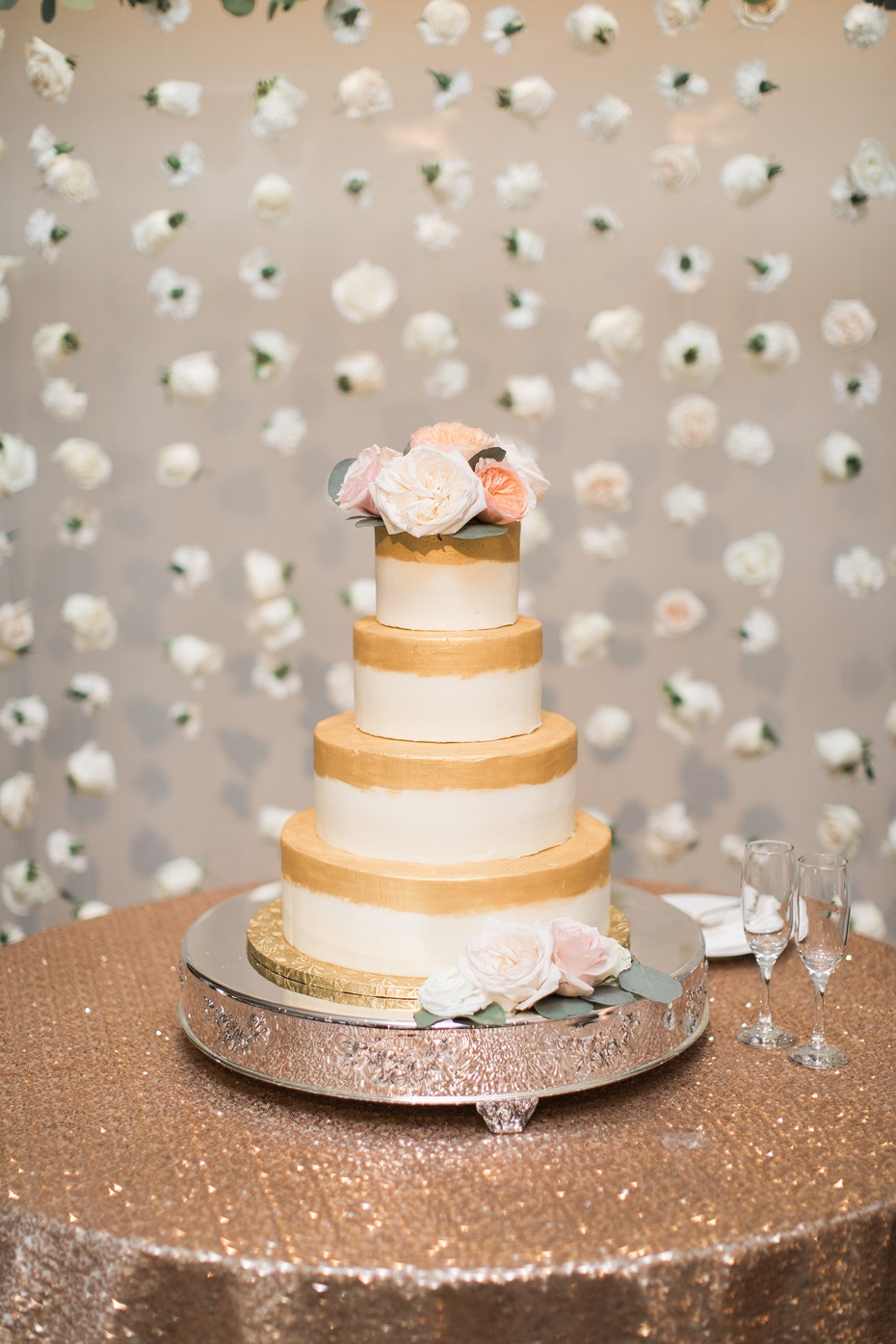 simple and sweet wedding cake with gold accents and a floating rose backdrop