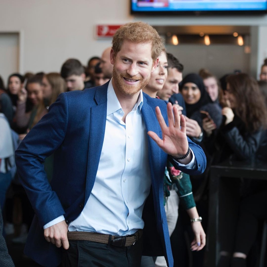 Prince Harry waving to a crowd in a blue suit