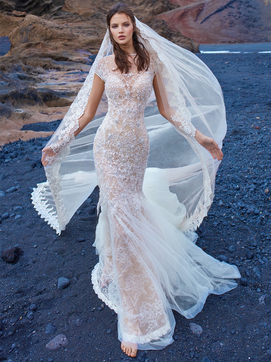 Stunning lace wedding gown with long veil on beach