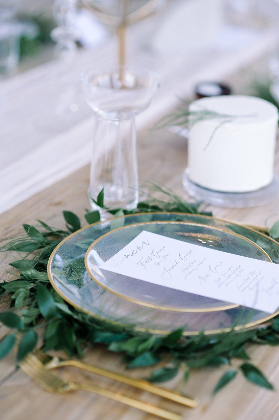 glass and gold place setting with greenery wreath charger
