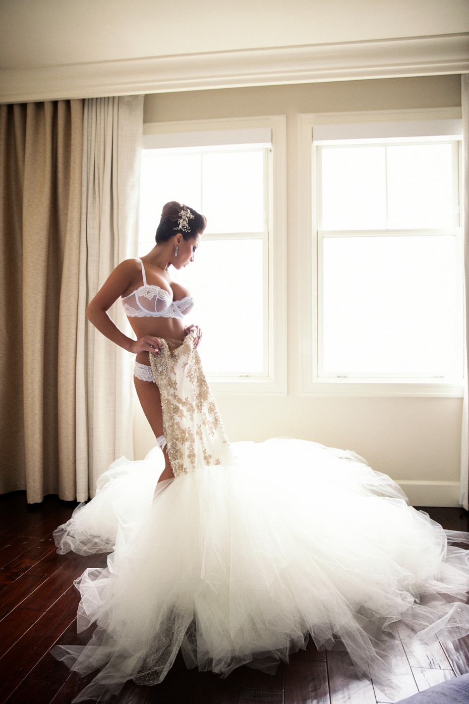 Bride in lingerie holding wedding dress by window light