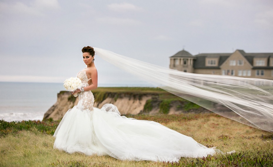 Bride in a stunning wedding dress with long veil near the ocean