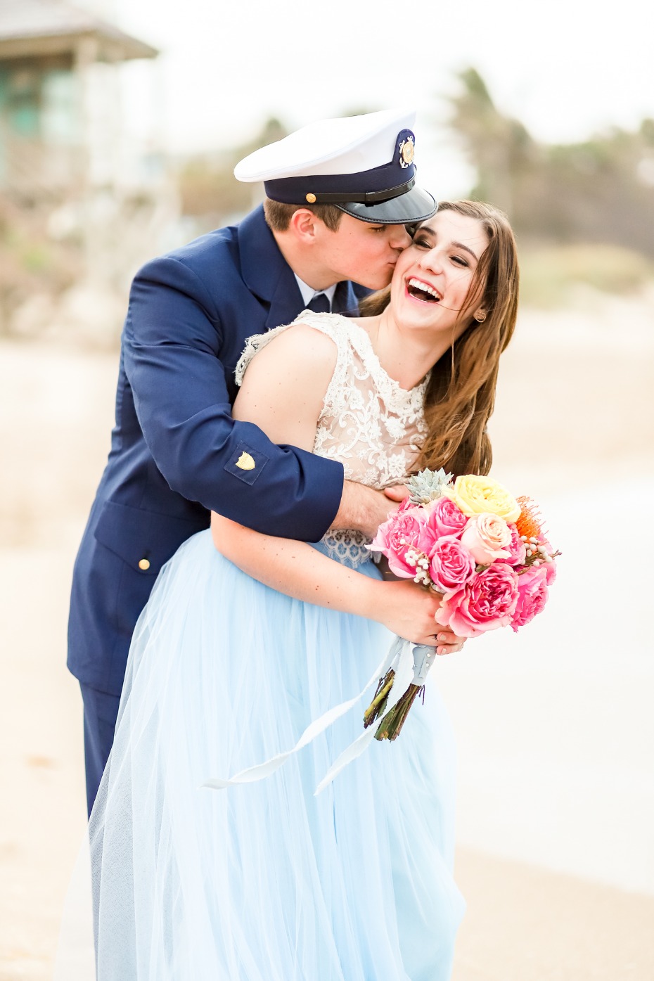 A happy couple shares a kiss on the beach with a beautiful bouquet