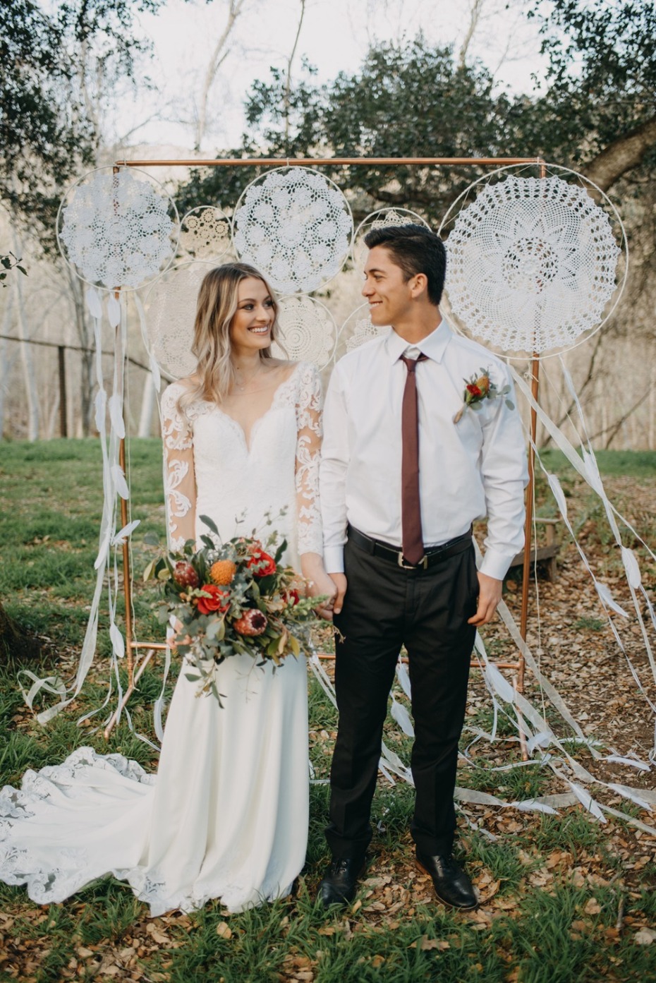 Boho wedding couple holding hands under dream catcher altar