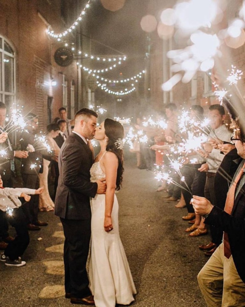 Newlyweds share a kiss as guests wave sparklers at their wedding