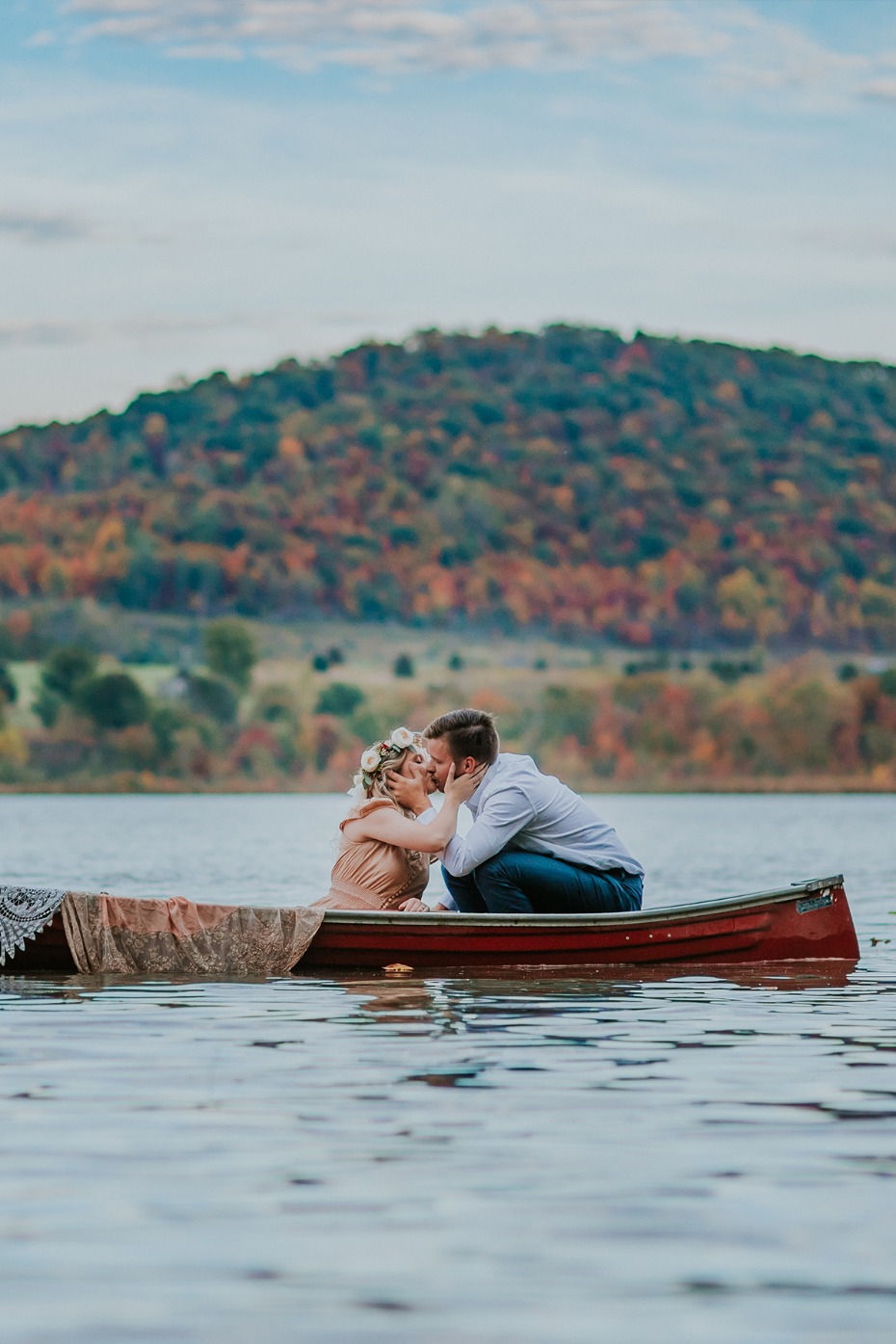 Couple kisses in canoe on lake with colorful fall trees