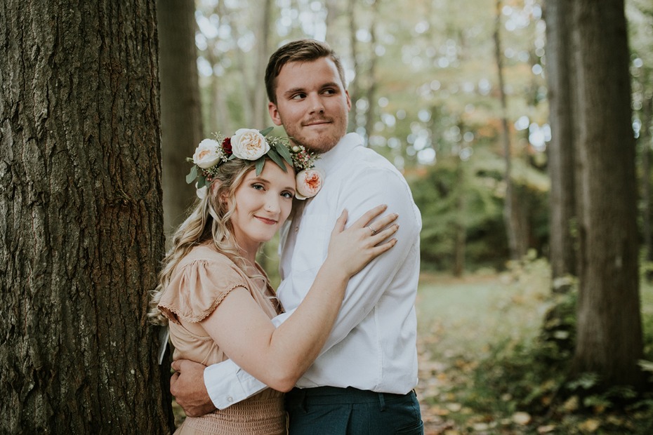 Engaged couple embraces near tree in romantic forest setting