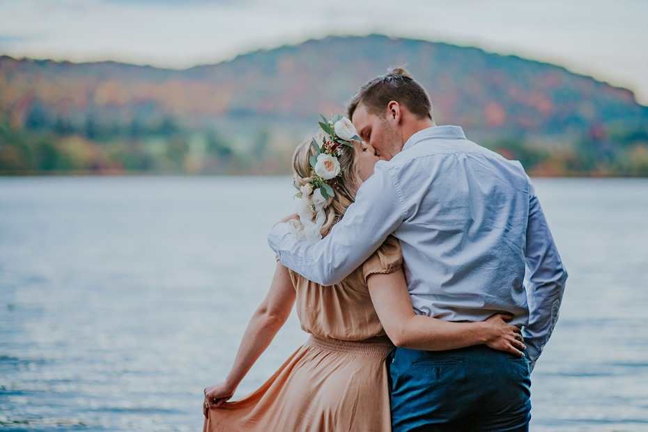 Romantic couple kissing by a lake with mountain backdrop