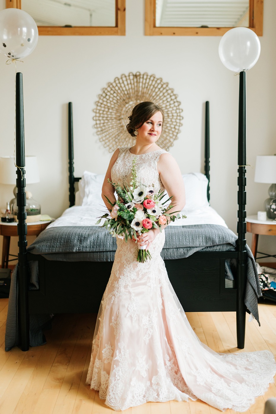 Bride in lace dress holding bouquet in bedroom setting