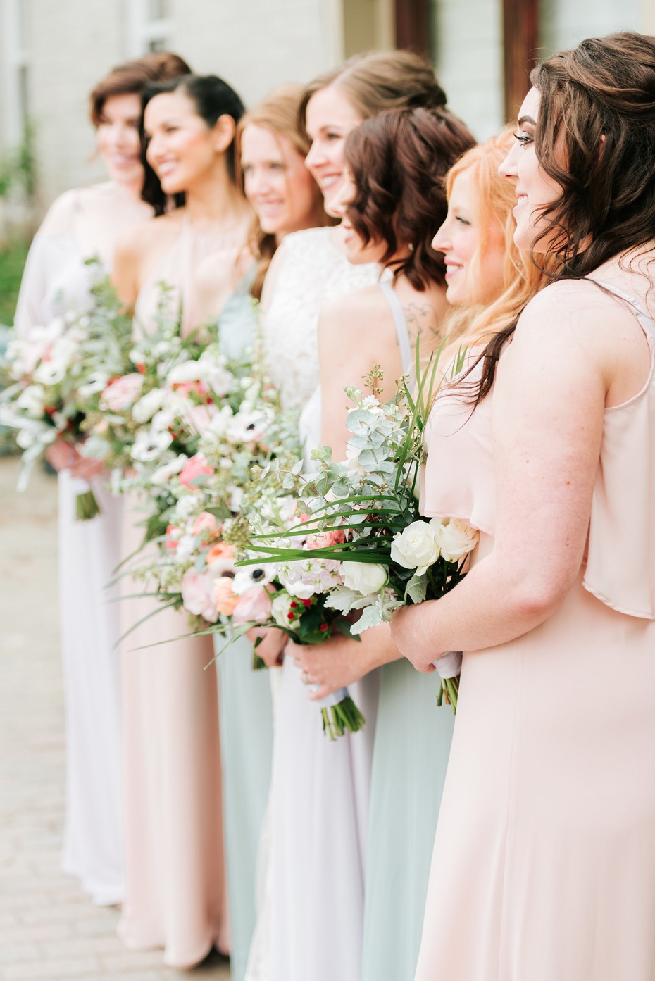 Bridesmaids in pastel dresses hold wedding bouquets
