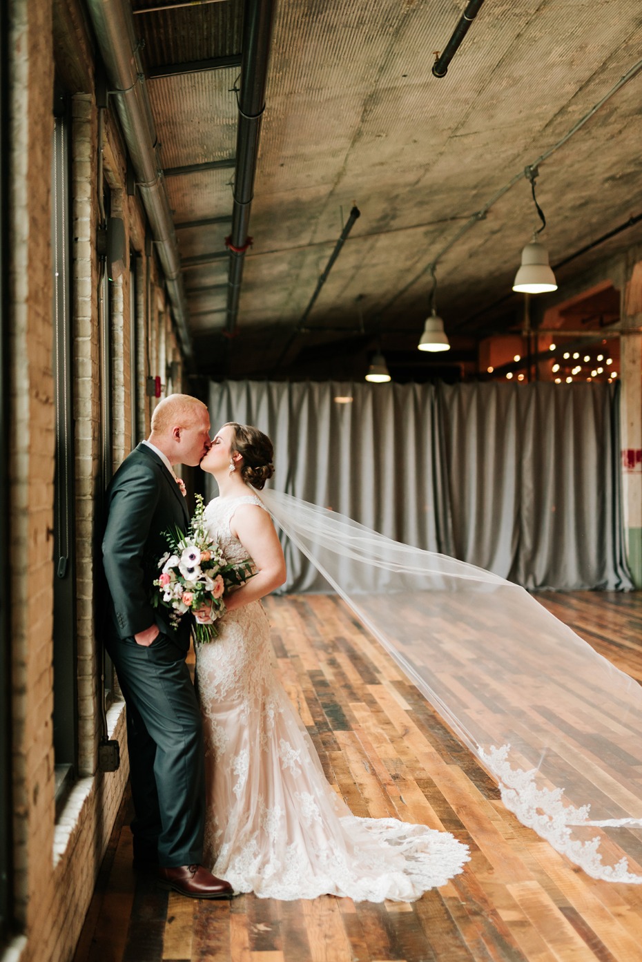 Bride and groom share a kiss by industrial windows