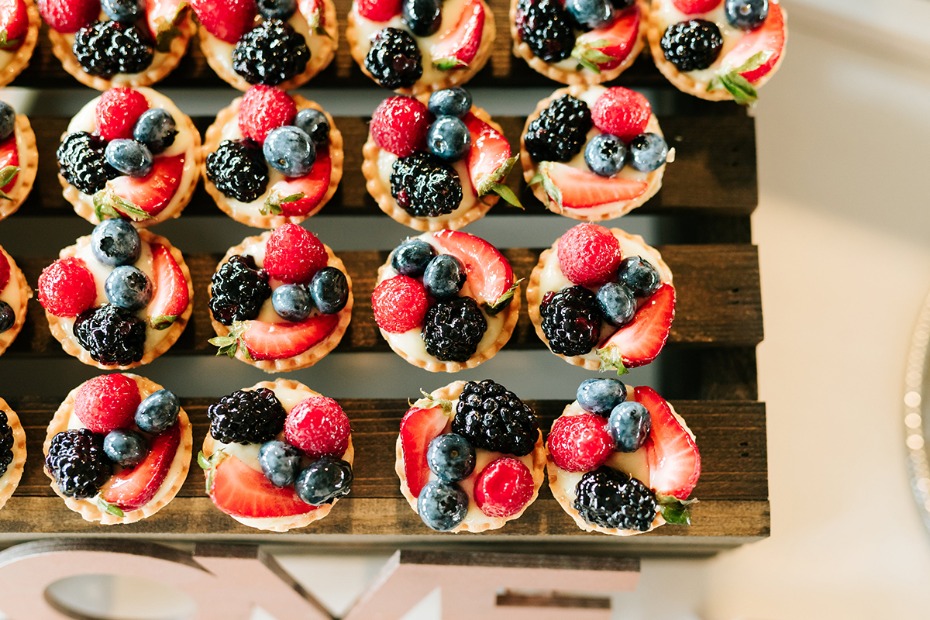 Berry topped mini tarts on a wooden display tray