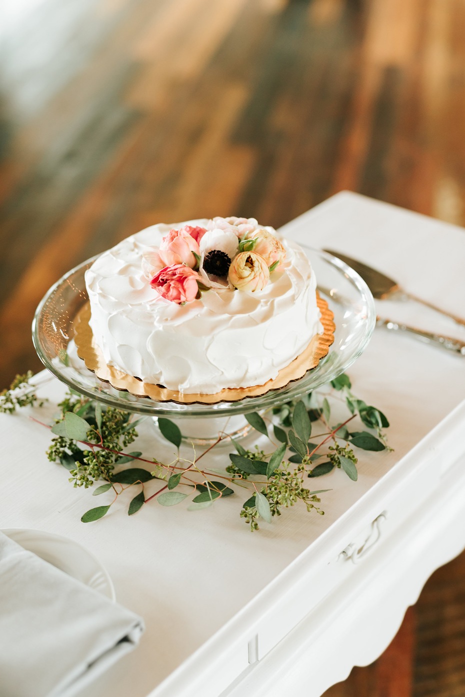 White cake with flowers on cake stand and eucalyptus