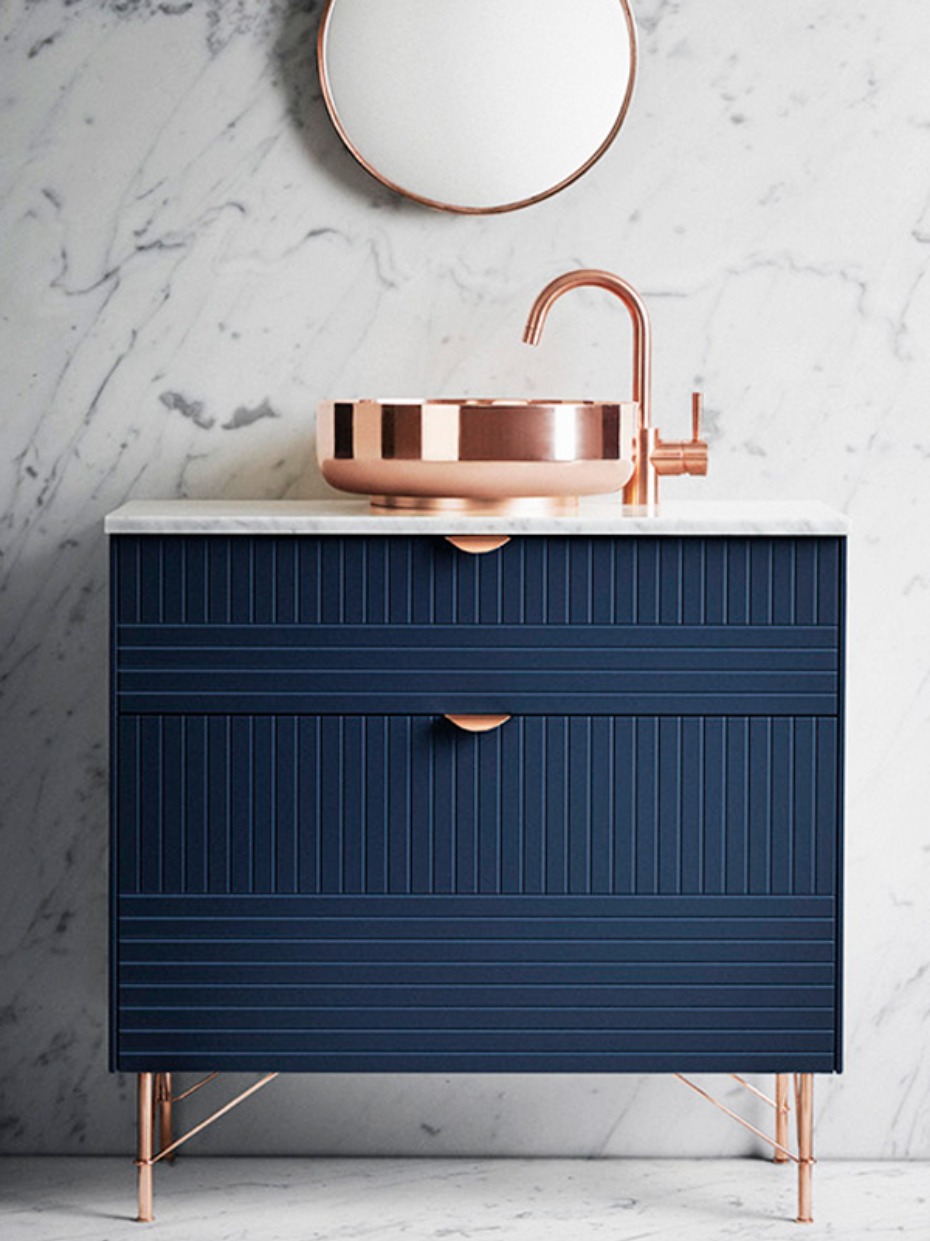 Modern blue vanity with copper accents and marble wall