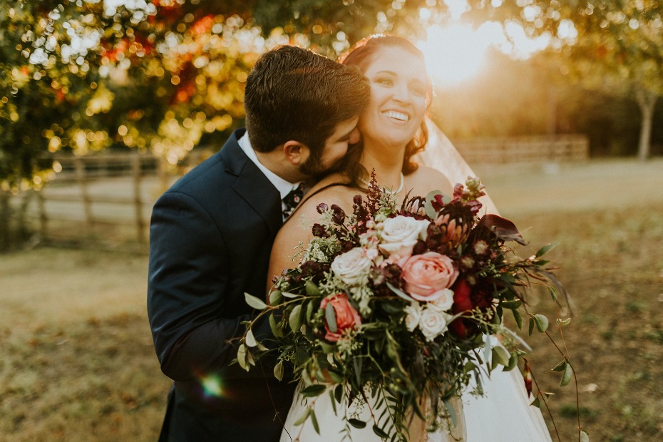 Bride smiling while groom embraces her on wedding day