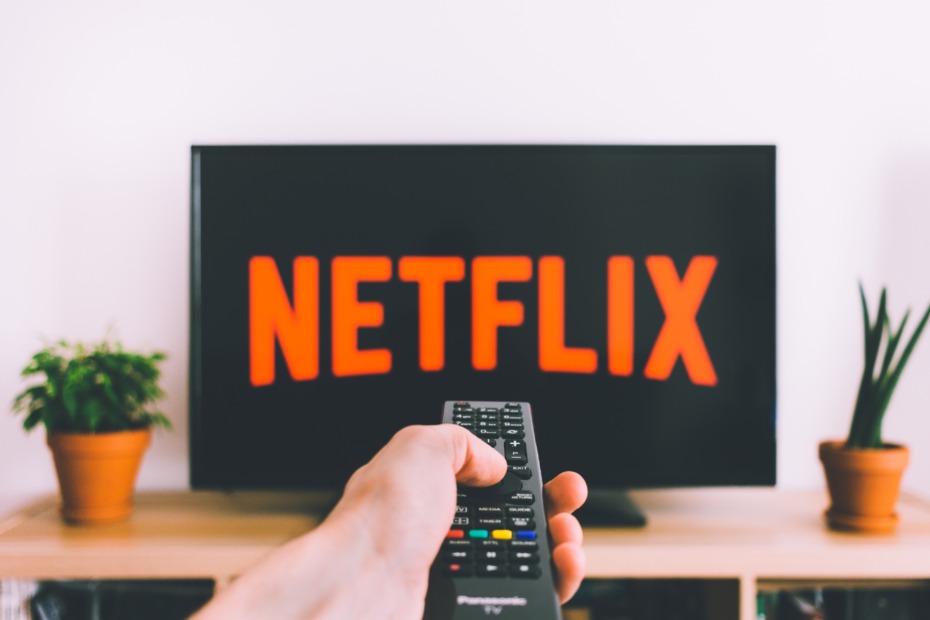 Hand using a remote to watch Netflix on a flat screen TV