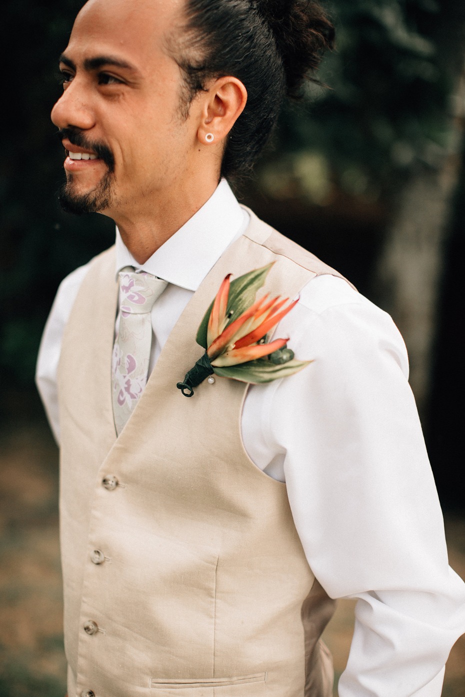 Groom in vest smiles wearing orange flower boutonniere