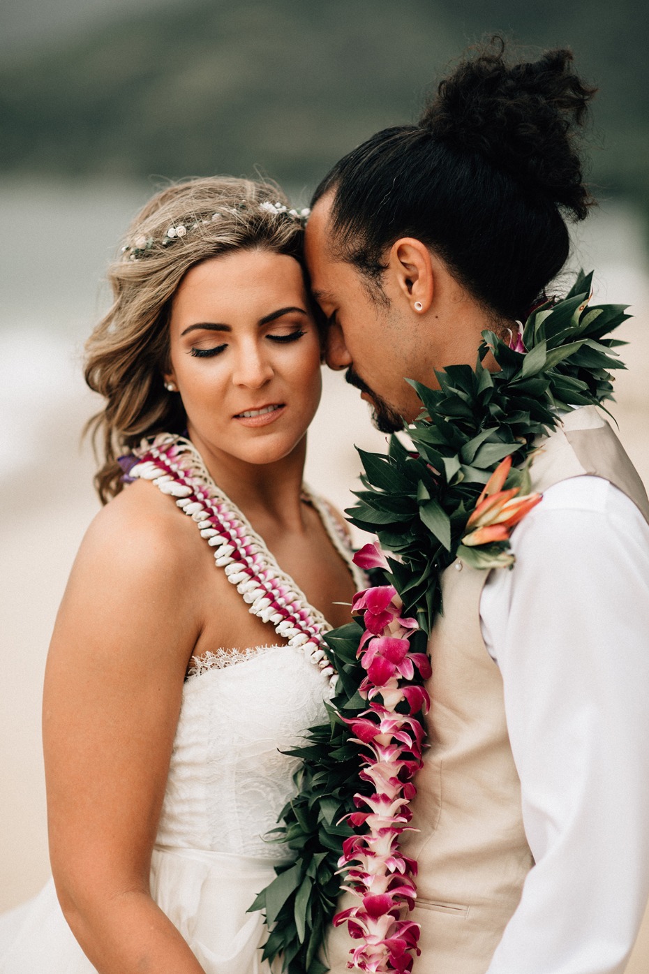 Bride and groom embrace wearing leis at beach wedding