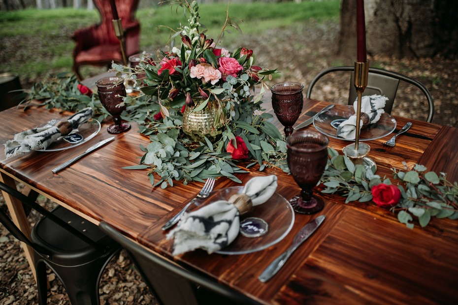 Wood table setting with red flowers and dark purple glasses
