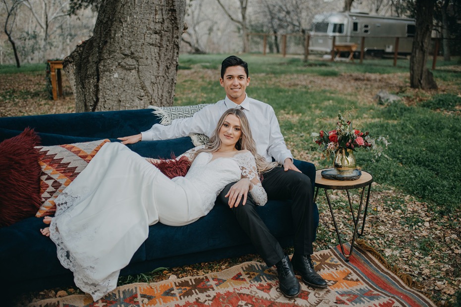 Bride and groom relax on bohemian outdoor lounge sofa