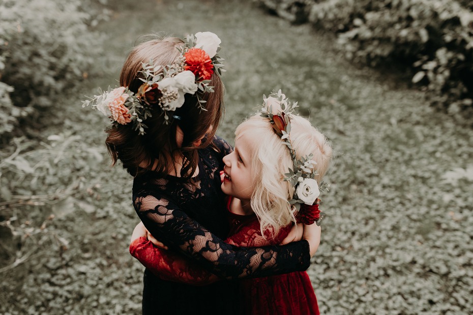 Two little girls hug wearing flower crowns outdoors