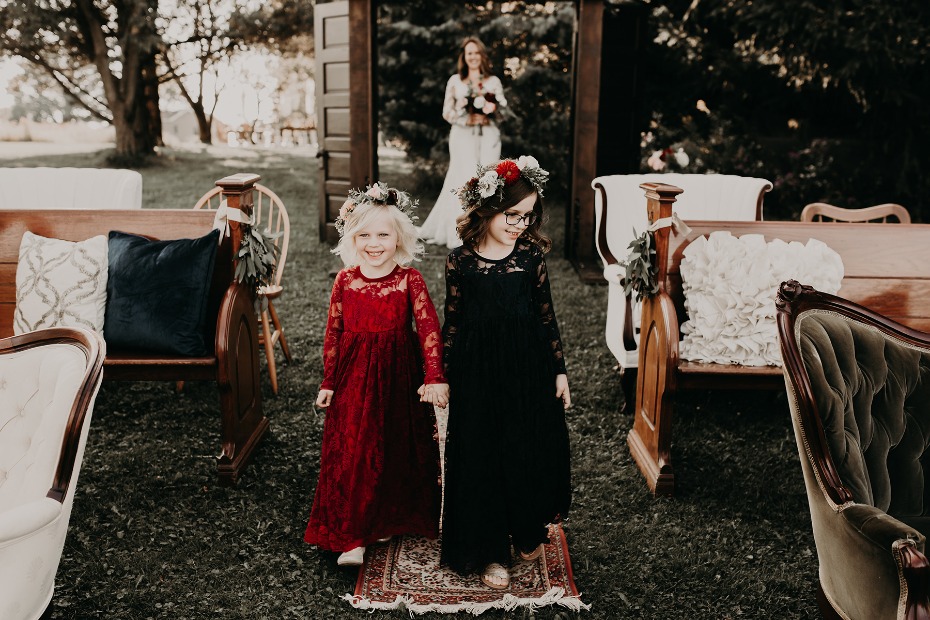 Flower girls walk down the aisle at a rustic wedding