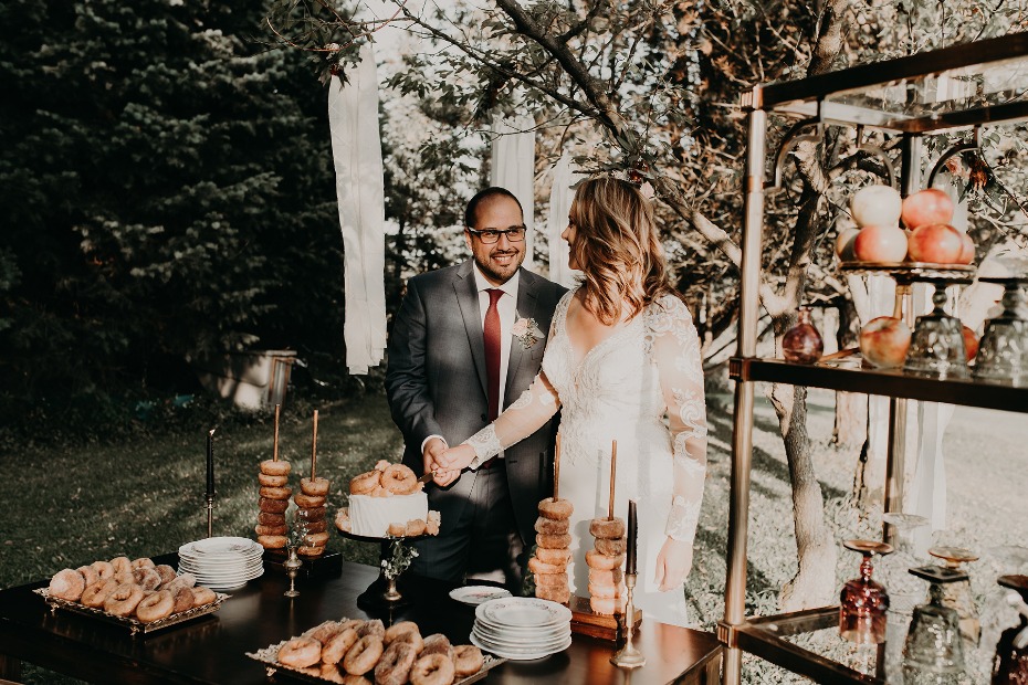 joyful wedding couple cuts cake surrounded by donuts