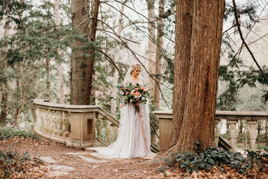 Bride with bouquet stands near old stone stairs in forest
