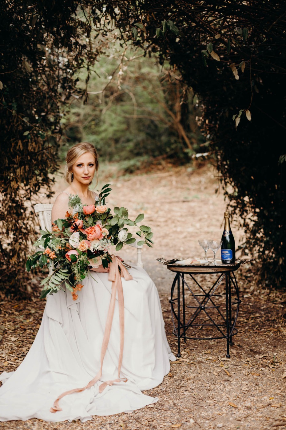 Blonde bride with bouquet awaits champagne in a garden