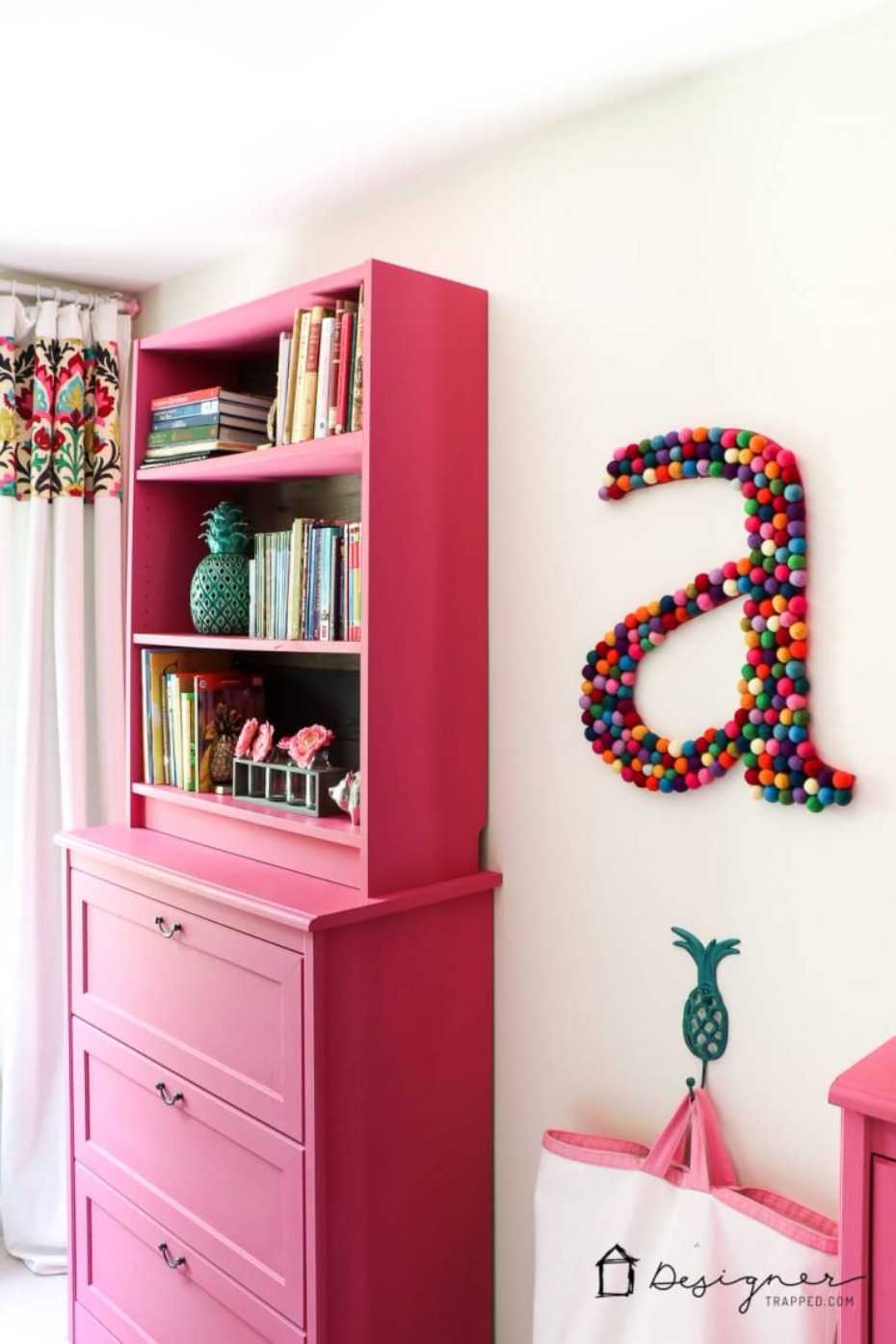Pink dresser with bookcase and colorful pompom wall art