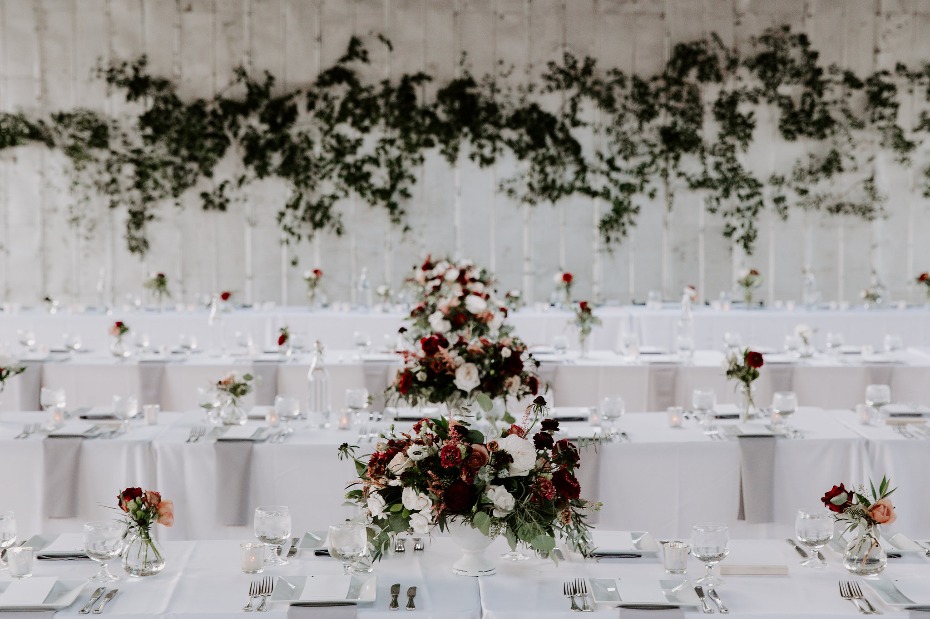 Blush and burgundy centerpieces with greenery wall