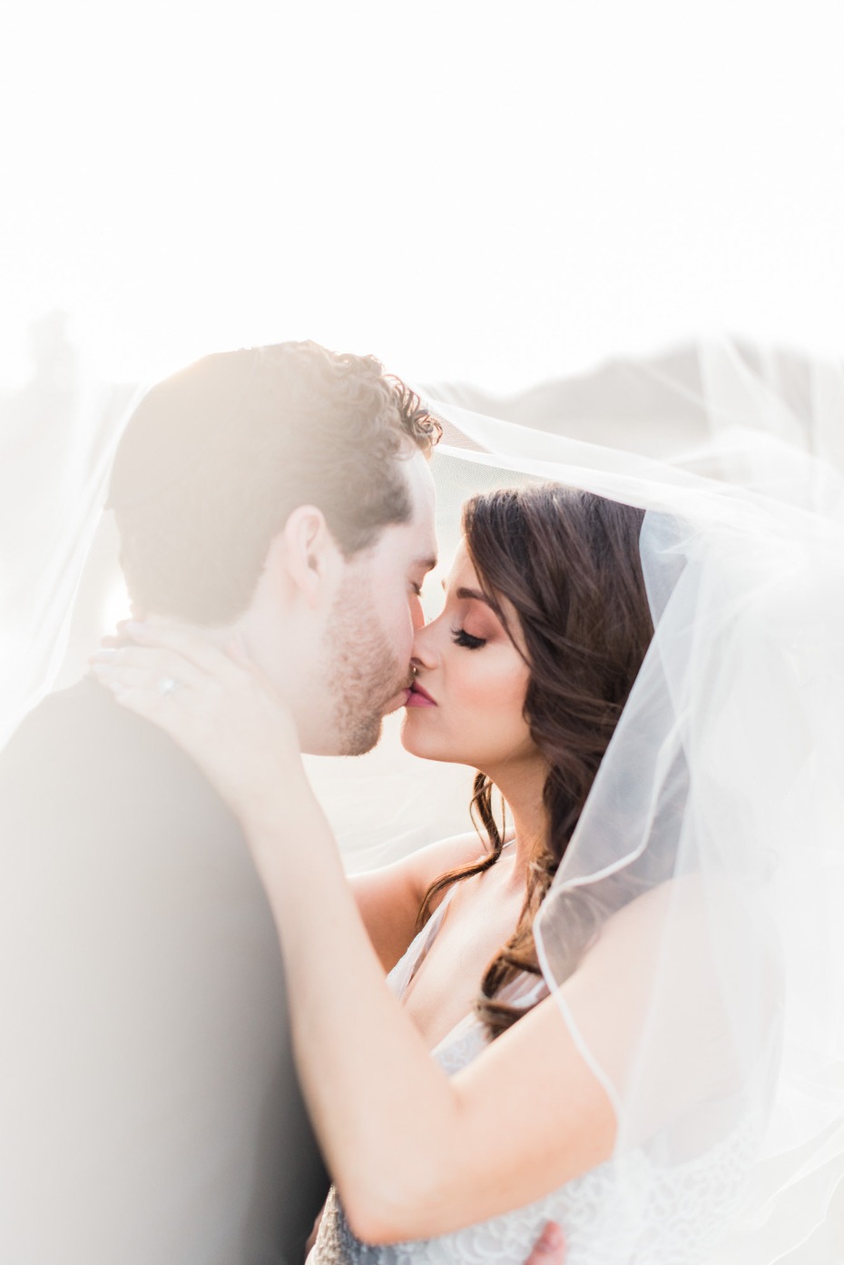 Bride and groom kissing tenderly, veiled in a soft, romantic light