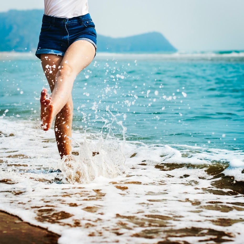 Woman walking barefoot on beach splashing in ocean water