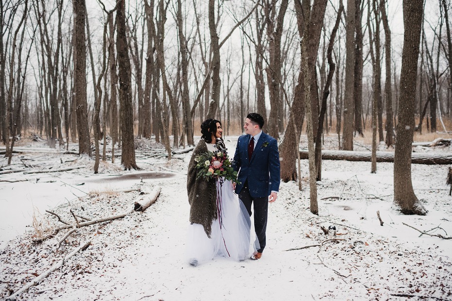 A newlywed couple strolls through a snowy winter forest, happy