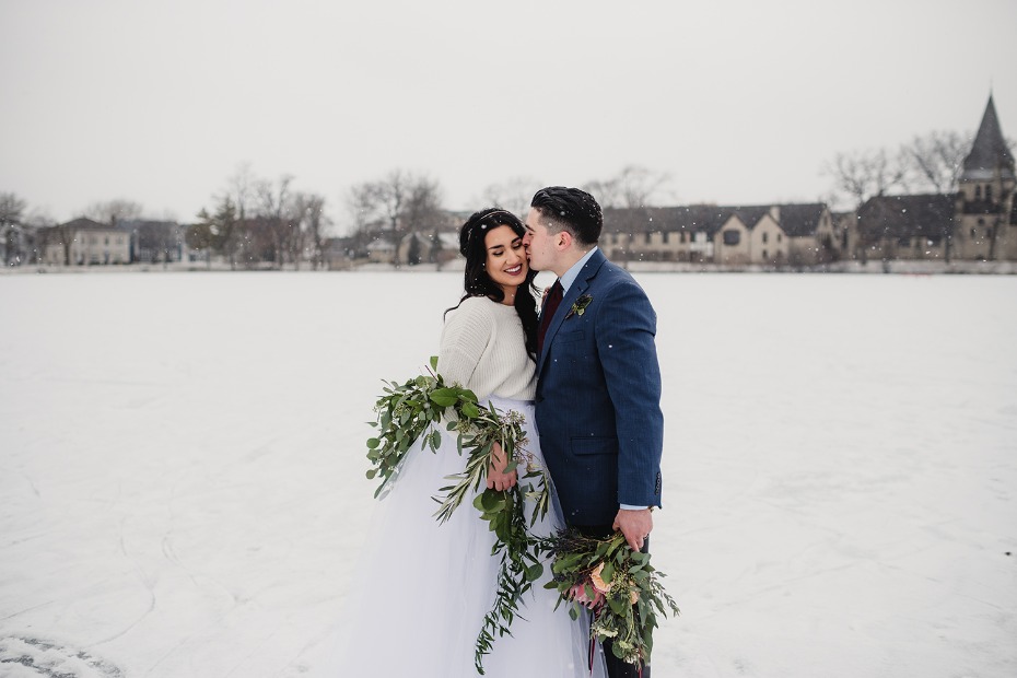 Couple kissing in winter wonderland wedding photo with bouquets
