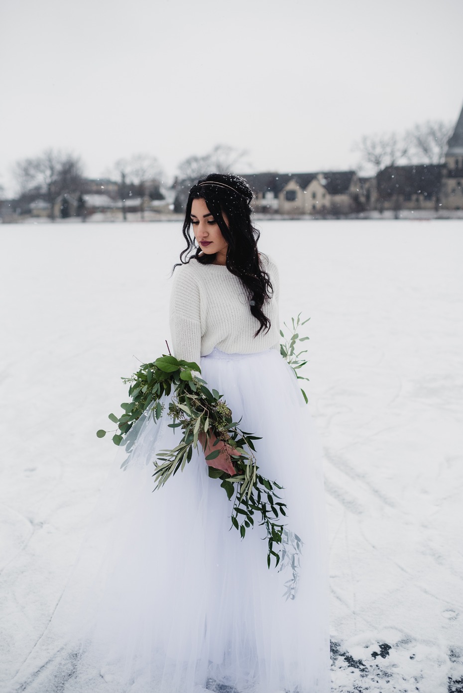 Winter bride in white dress holding greenery bouquet