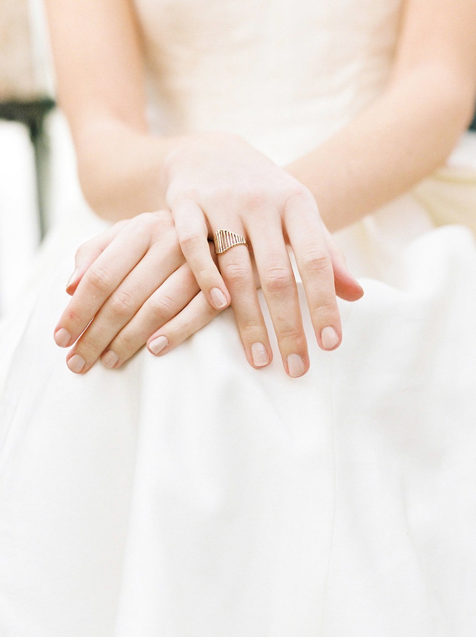 Bride wears minimalist gold wedding ring on white dress