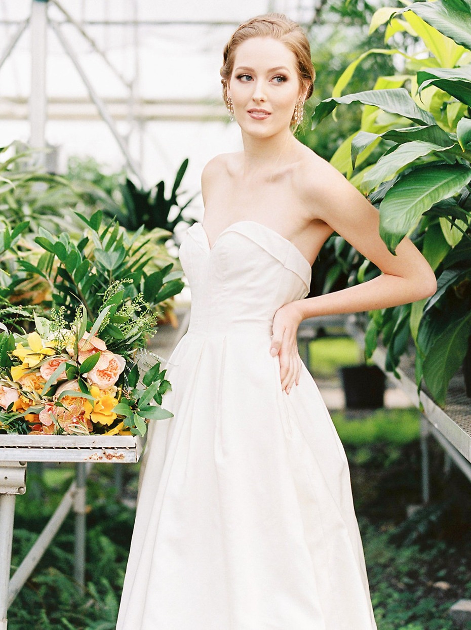 Bride in strapless gown poses in lush greenhouse