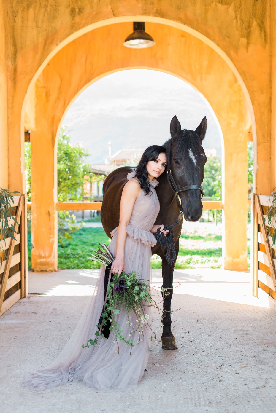 Woman in gown with black horse at stable entrance